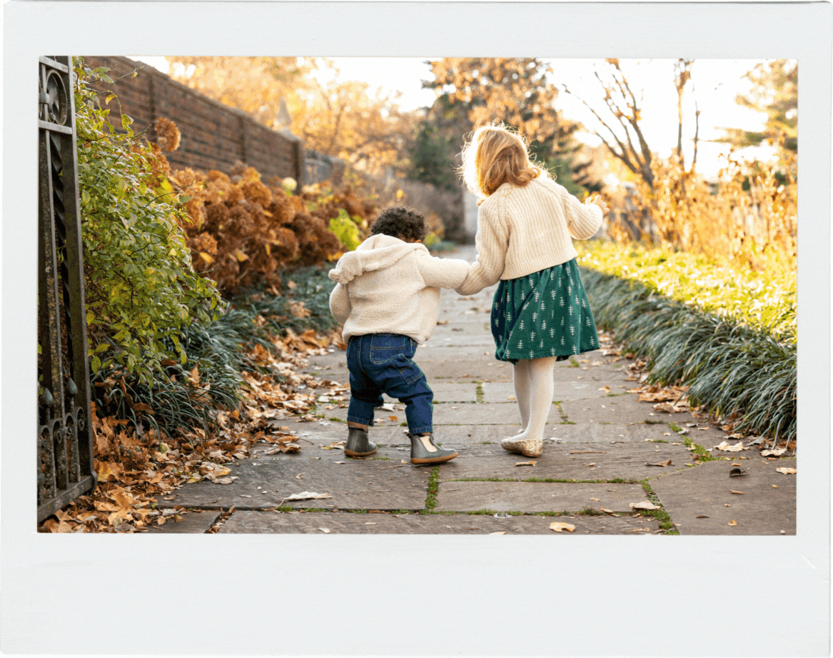Big sister holds her toddler brother's hand as he walks down the sidewalk