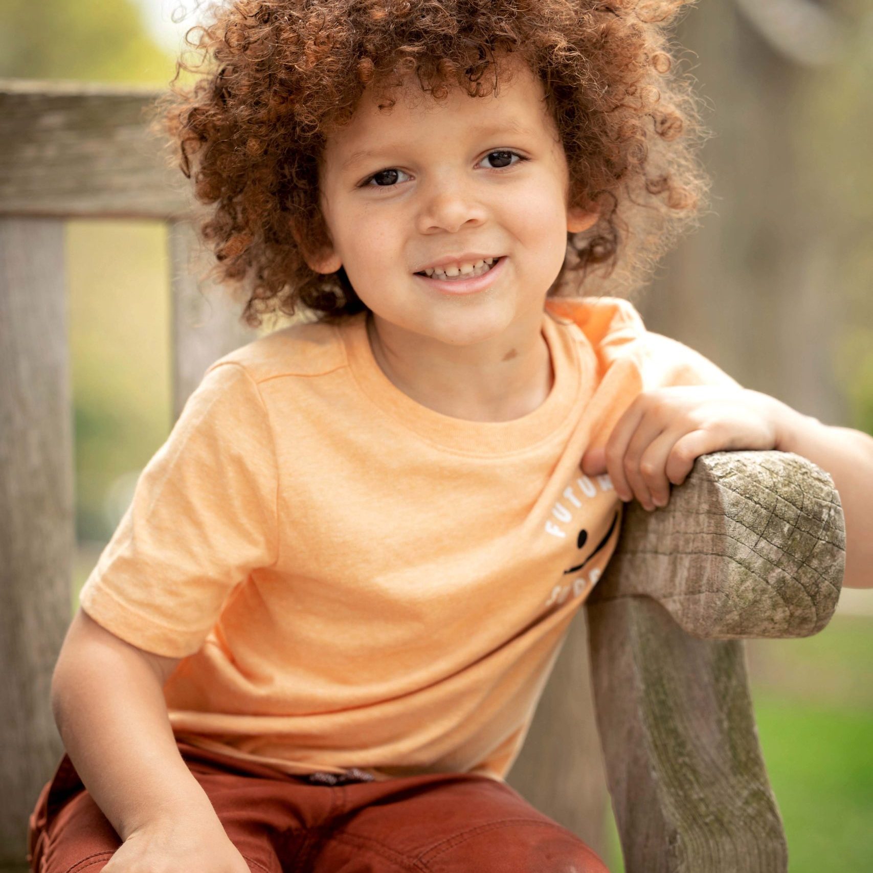 Boy with curly hair sitting on a bench outside The Frick mansion in Pittsburgh, PA