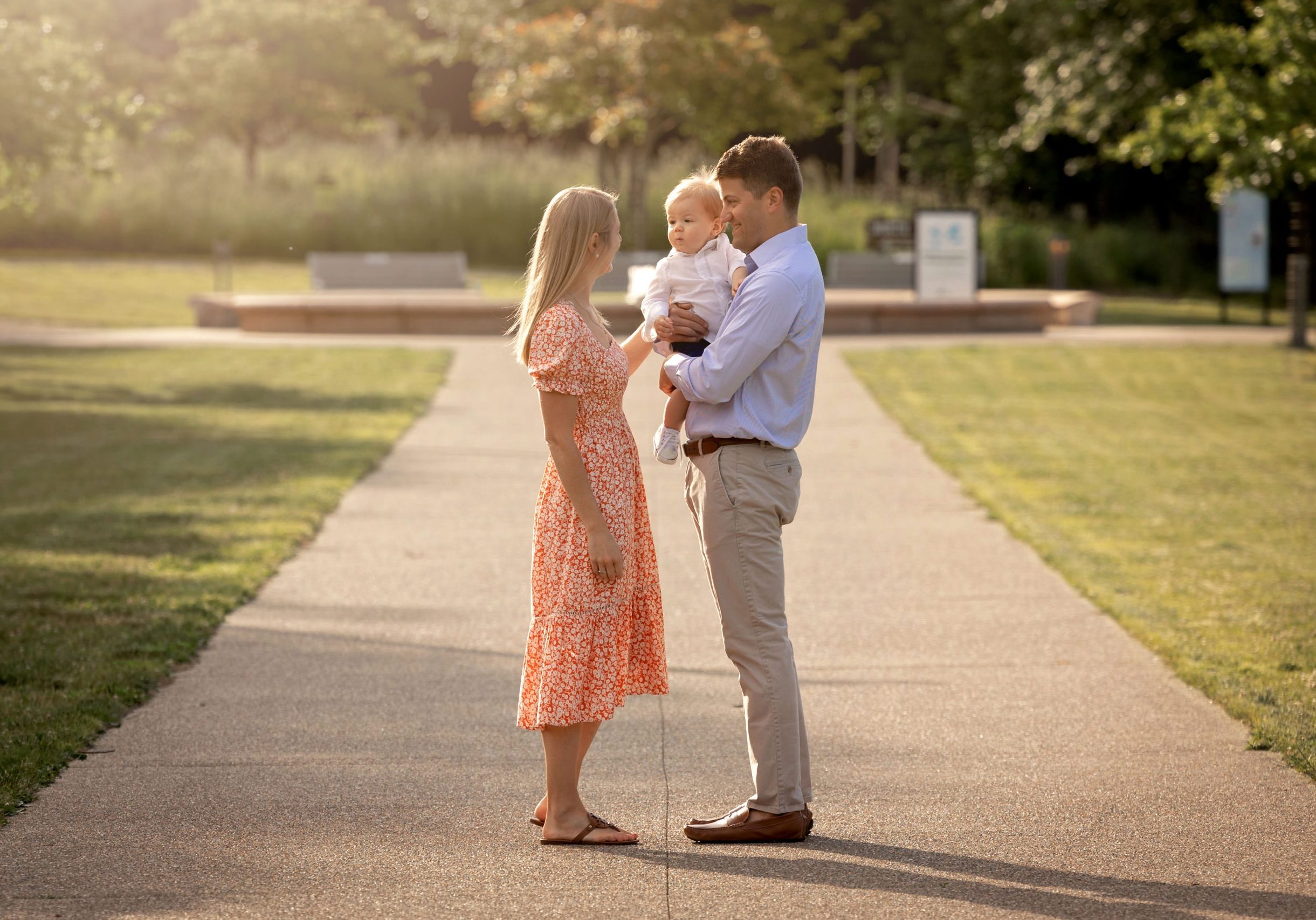 A morning photo shoot provides a hazy backdrop for mom and dad to hold their toddler in front of the fountain in Frick Park